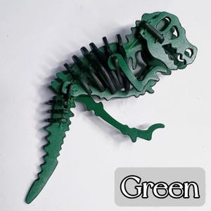 May include: A green dinosaur skeleton puzzle with black accents. The puzzle is made of interlocking pieces and features a detailed design of a Tyrannosaurus Rex. The word "Green" is displayed in a white font on a gray background.
