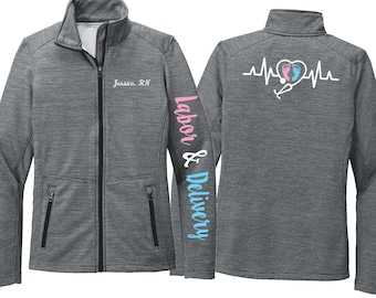 May include: A gray zip-up jacket with the text "Labor & Delivery" on the sleeve in pink and blue. The front of the jacket has the name "Jessica, RN" embroidered. The back features a heartbeat design with a stethoscope and a heart.
