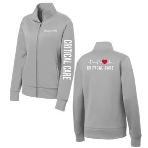 Peut inclure: Veste zippée gris clair avec le texte "Morgan, RN" sur la poitrine et "CRITICAL CARE" imprimé verticalement sur la manche gauche. Le dos de la veste présente un graphique de battement de cœur avec un cœur rouge et les mots "CRITICAL CARE".
