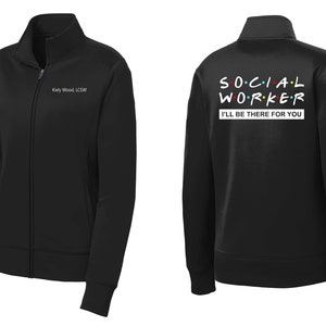 May include: Black zip-up jacket with the text "SOCIAL WORKER" in a colorful font and the phrase "I'LL BE THERE FOR YOU" below it. The jacket has a name tag on the left side with the text "Kelly Wood, LCSW".