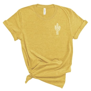 Puede incluir: Una camiseta amarilla con un gr&aacute;fico de cactus blanco en la parte delantera.