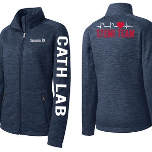 May include: A navy blue fleece jacket with a white "Cath Lab" print on the left sleeve and a red heart with a white EKG line and "STEMI TEAM" text on the back. The jacket has a zipper closure and two pockets.