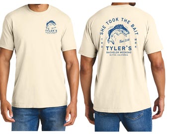 Op de afbeelding: Crèmekleurig T-shirt met blauwe grafische prints. De voorkant heeft een visontwerp en de tekst "Tyler's Bachelor Weekend". De achterkant toont een grotere visafbeelding met de tekst "She Took the Bait" en "Tyler's Bachelor Weekend, Blythe, California."