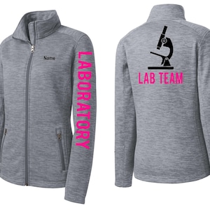 Peut inclure: Veste grise zippée avec le mot "LABORATORY" imprimé verticalement en rose sur la manche gauche. L'avant de la veste comporte une petite poche et le mot "Name" imprimé au-dessus de la fermeture éclair. Le dos de la veste présente un microscope et les mots "LAB TEAM" en rose.