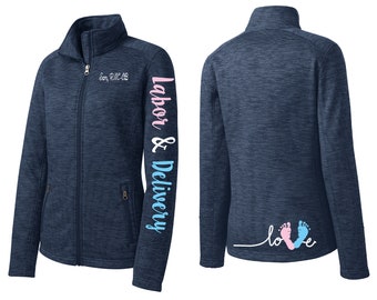 May include: Navy blue zip-up jacket with the words "Labor & Delivery" in pink and blue on the sleeve. The jacket has a high collar and a zipper closure. The back of the jacket features the word "love" with pink and blue footprints.