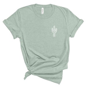 Puede incluir: Una camiseta verde claro con un contorno blanco de un cactus en la parte delantera.