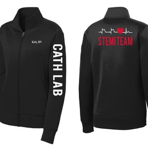 May include: Black zip-up jacket with white text on the sleeve that reads "Cath Lab" and white text on the front that reads "Kiley, RN". The back of the jacket has a red heart and EKG line with the text "STEMI TEAM".