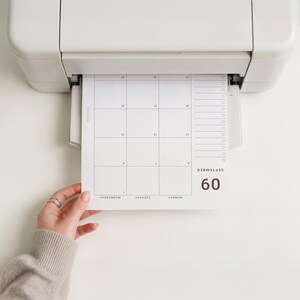 May include: A white printer outputting a paper calendar page for September. The calendar features a grid layout with numbered dates, a vertical checklist column on the right side, and the text September 09 printed in bold black font.