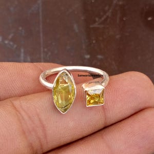 May include: Open-style silver ring featuring two yellow gemstones. One gemstone is a marquise cut, and the other is a square cut. The ring has a modern, minimalist design. The text "SanwariaJewellers" is visible on the ring.