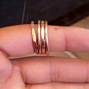 Puede incluir: Colección de cinco anillos de color cobre con diferentes texturas y diseños. Los anillos están apilados en un dedo, mostrando sus diferentes acabados. Los anillos están hechos de un material metálico brillante.