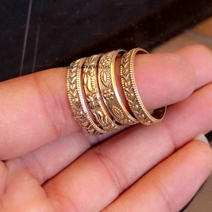 Op de afbeelding: Een verzameling goudkleurige ringen, elk met een uniek, gedetailleerd bloemen- en geometrisch patroon. De ringen worden op een vinger getoond, waarbij hun ingewikkelde ontwerpen worden getoond. De ringen zijn van POSHPALATAJEWELLERS.