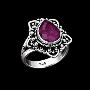 Op de afbeelding: Een ring van sterling zilver met een peervormige, gefacetteerde dieproze robijn, gezet in een decoratief frame met kralen en gedraaide draaddetails. De ringband is gestempeld met 925, wat de samenstelling van het sterling zilver aangeeft.