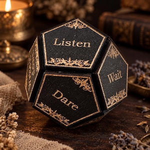 Può includere: Un oggetto nero a forma di dodecaedro con bordi dorati e dettagli ornamentali agli angoli. Ogni faccia pentagonale presenta testo dorato, incluse le parole Listen, Wait e Dare, stampate in un carattere serif sulla superficie nera opaca.