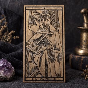 May include: A rectangular wooden plaque featuring a laser-engraved illustration of the High Priestess tarot card. The design includes the Roman numeral II at the top, the figure wearing a papal tiara holding a book, and the text LA PAPESSE.