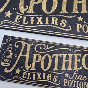 May include: Two wooden signs with the word "APOTHECARY" in gold lettering. The signs are black with gold accents, stars, and the words "ELIXIRS" and "POTIONS". One sign also includes a bottle illustration.