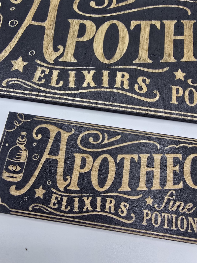 May include: Two wooden signs with the word "APOTHECARY" in gold lettering. The signs are black with gold accents, stars, and the words "ELIXIRS" and "POTIONS". One sign also includes a bottle illustration.