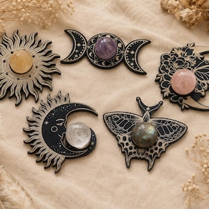 May include: Five decorative wooden plaques featuring intricate black line art designs including a sun, a triple moon symbol, a floral crescent moon, a crescent moon with a face, and a moth, each centred with a polished gemstone sphere.