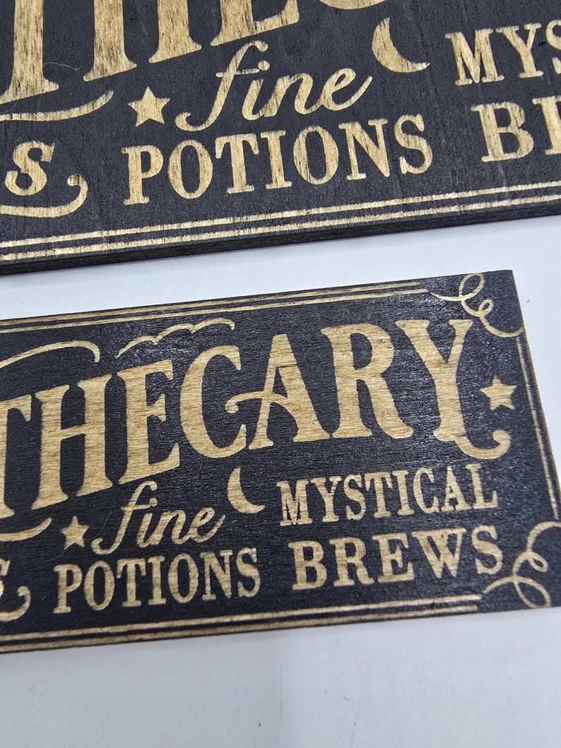 May include: Two rectangular wooden signs with gold lettering on a black background. The top sign reads "fine POTIONS BREWS" and the bottom sign reads "APOTHECARY fine MYSTICAL POTIONS BREWS". Decorative stars and crescent moons are included.