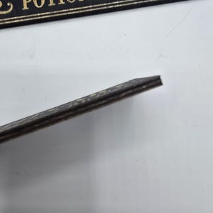 May include: A black wooden sign with gold lettering that reads "fine potions brews". The sign has a dark, textured edge. The background is white.