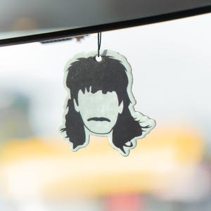 Puede incluir: Ambientador en blanco y negro con forma de corte de pelo mullet. Cuelga de un cord&oacute;n negro. El fondo est&aacute; borroso, con suaves tonos amarillos y blancos.