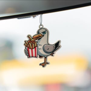May include: A cartoon-style air freshener featuring a seagull holding a container of french fries. The seagull is primarily white and gray with an orange beak and feet. The fries are golden brown, and the container has red and white stripes.