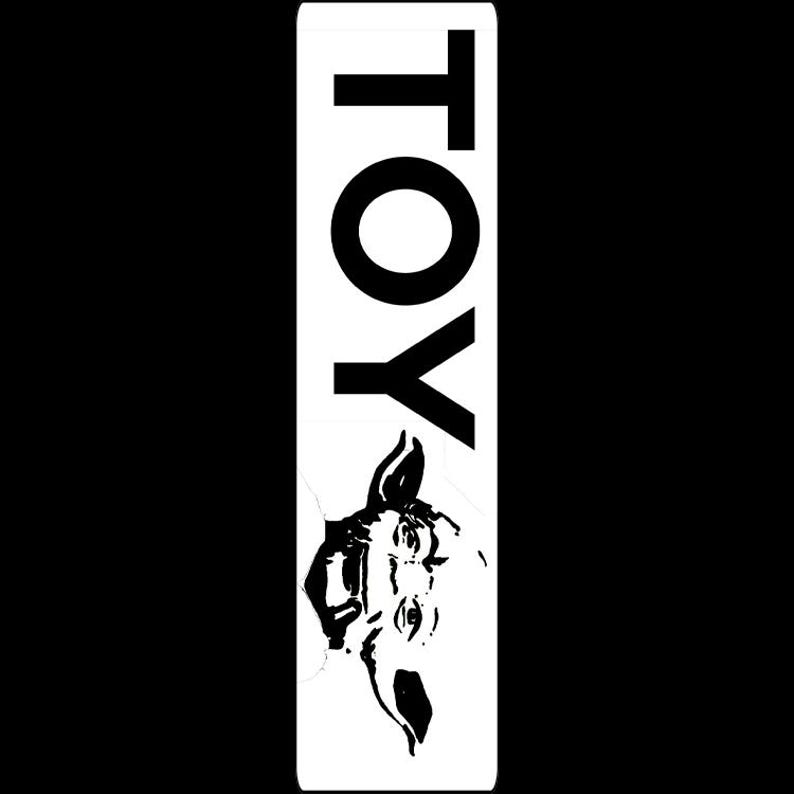 May include: A vertical white rectangle with the word "TOY" in bold black letters at the top. Below the text is a black and white illustration of a horse's head. The background is solid black.