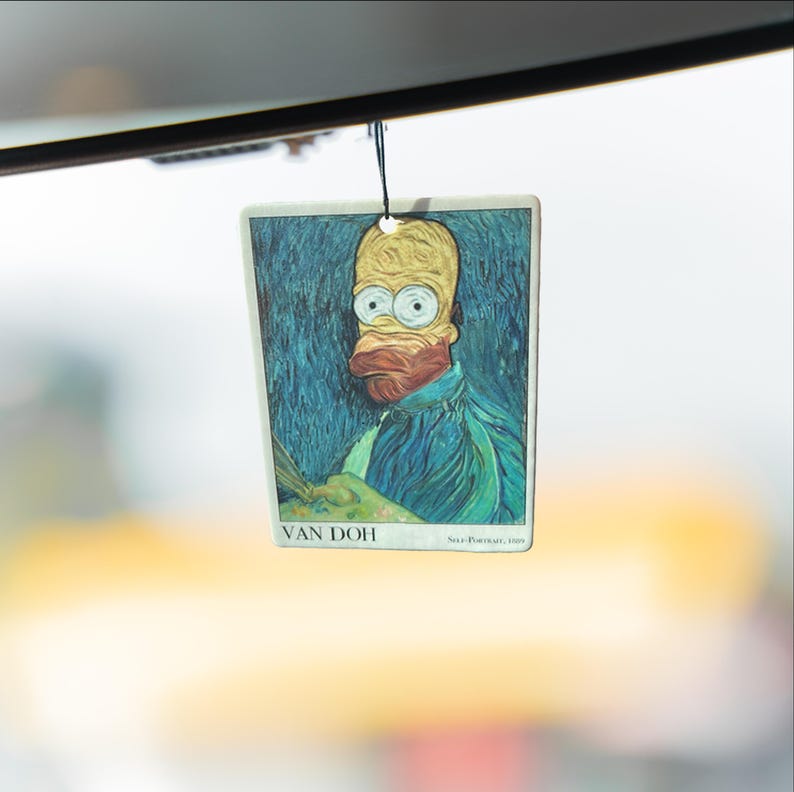 May include: Rectangular air freshener featuring a parody of Van Gogh's self-portrait with Homer Simpson's face. The artwork is set against a blue background with the text "VAN DOH" at the bottom. The air freshener hangs from a black string.