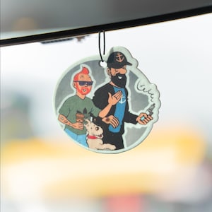 May include: A round, car air freshener featuring cartoon characters. One character has red hair and sunglasses, the other has a black beard and a captain's hat. A white dog with a red collar is also featured.