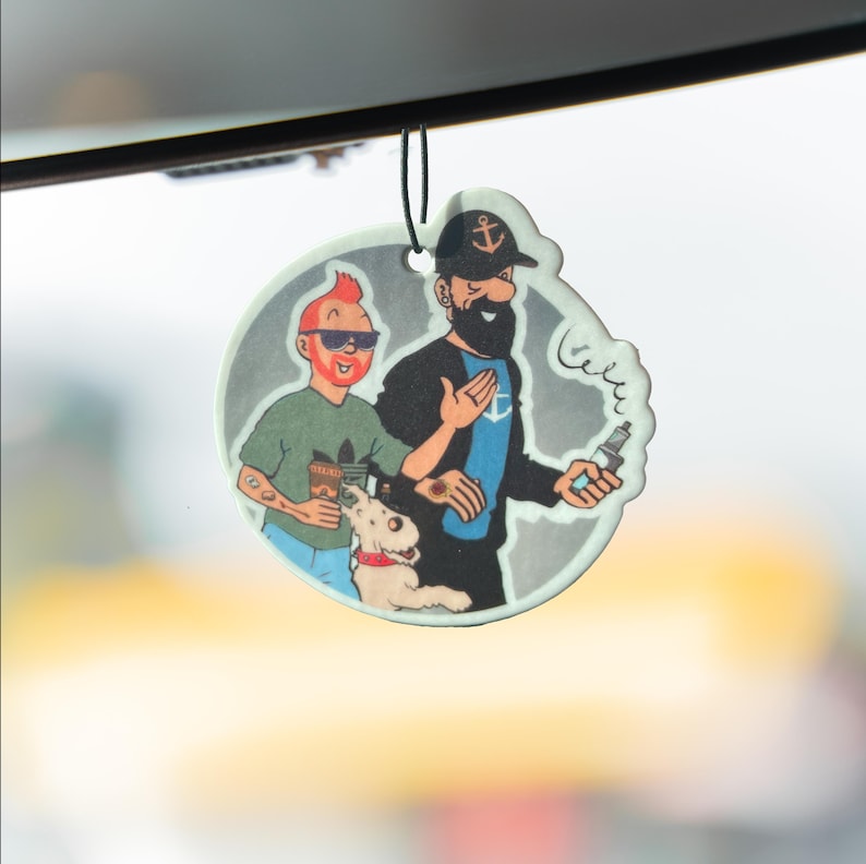 May include: A round, car air freshener featuring cartoon characters. One character has red hair and sunglasses, the other has a black beard and a captain's hat. A white dog with a red collar is also featured.