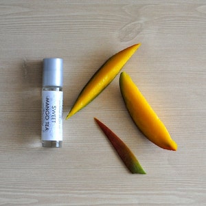 May include: A silver roller bottle with a white label that reads "Sweet Mango Tea" on a wooden surface with three yellow mango slices.