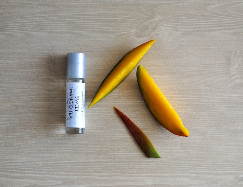 May include: A silver roller bottle with a white label that reads "Sweet Mango Tea" on a wooden surface with three yellow mango slices.