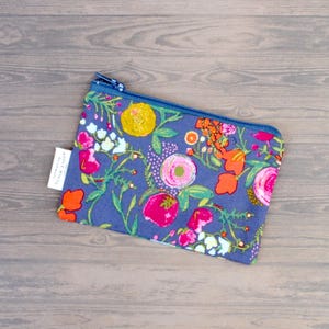 May include: A floral print pouch with a blue zipper. The pouch features a pattern of pink, orange, and yellow flowers on a blue background. A small white tag is attached to the side. The pouch is rectangular in shape.