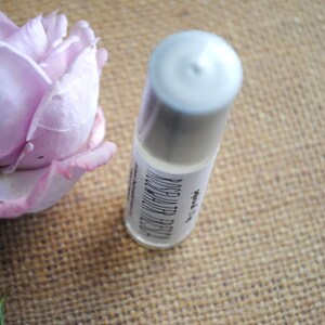 Op de afbeelding: Een witte roll-on fles met een zwart label waarop "ROSEWATER TONER" en "SKINCARE BY" staat.