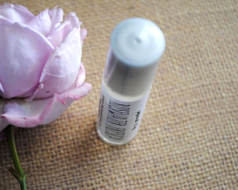 Op de afbeelding: Een witte roll-on fles met een zwart label waarop "ROSEWATER TONER" en "SKINCARE BY" staat.