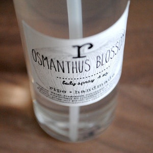 Pu&ograve; includere: Una bottiglia di vetro trasparente con un'etichetta bianca che dice "Osmanthus Blossom body spray 4 oz ripe - handmade".