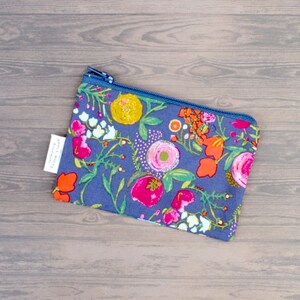 May include: A floral print pouch with a blue zipper. The pouch features a vibrant pattern of pink, orange, and yellow flowers on a blue background. A small white tag is attached to the side.