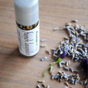 May include: A clear glass bottle with a white label that reads "French Lavender" and a brown liquid inside. The bottle is sitting on a wooden surface with dried lavender flowers scattered around it.