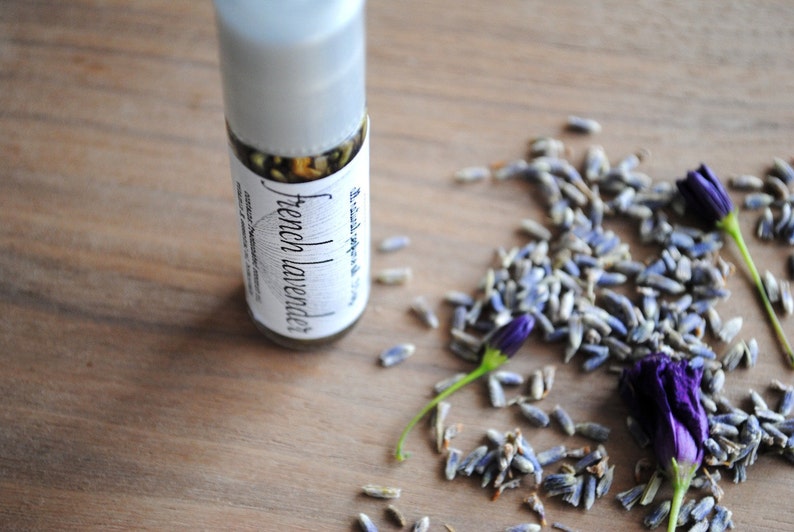 May include: A clear glass bottle with a white label that reads "French Lavender" and a brown liquid inside. The bottle is sitting on a wooden surface with dried lavender flowers scattered around it.