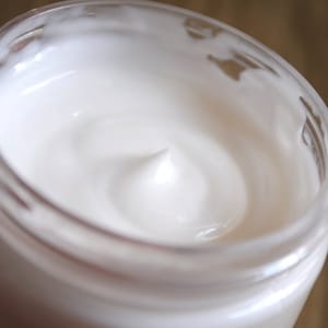 Könnte beinhalten: Nahaufnahme einer weißen Creme in einem durchsichtigen Glas. Die Creme ist glatt und hat ein Wirbelmuster.