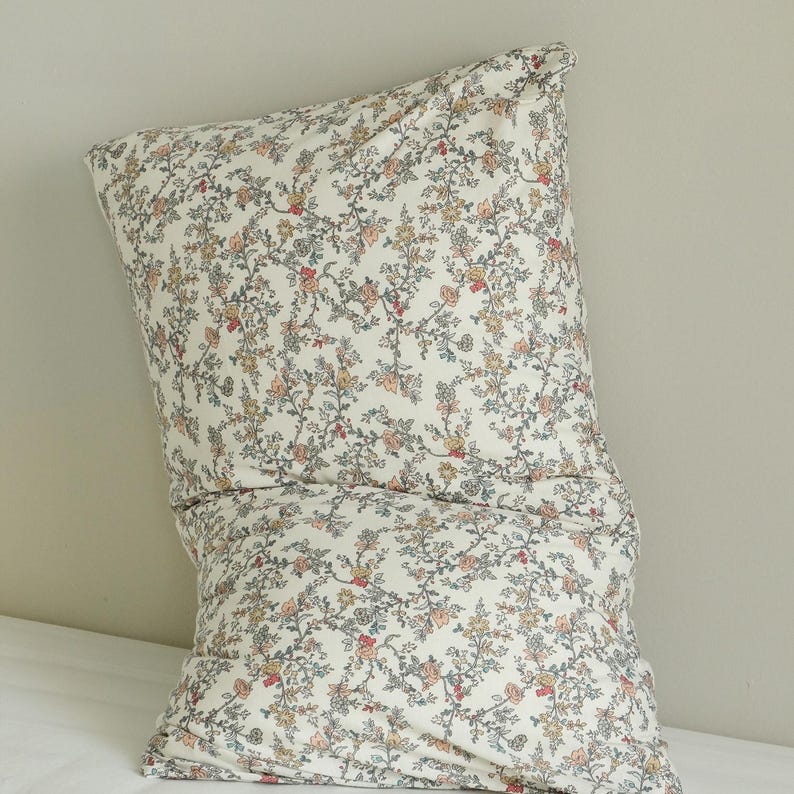 May include: A floral patterned pillow with a cream background. The pattern features small flowers in shades of pink, yellow, and blue. The pillow is rectangular and appears to be made of soft fabric, perfect for a bedroom or living room.