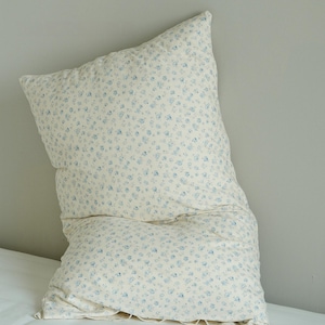 May include: A large, rectangular pillow with a cream-colored background and a pattern of small blue floral designs. The pillow is slightly crumpled, suggesting a soft, comfortable texture, and is placed on a white surface.