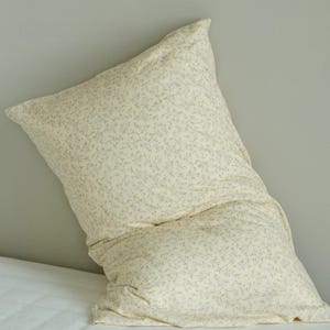 May include: A large, cream-colored pillow with a floral pattern of small, light blue and green flowers. The pillow is slightly rumpled, suggesting comfort and use. The pillow is on a white surface.