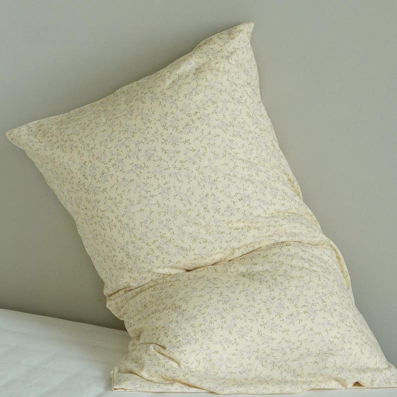 May include: A large, cream-colored pillow with a floral pattern of small, light blue and green flowers. The pillow is slightly rumpled, suggesting comfort and use. The pillow is on a white surface.