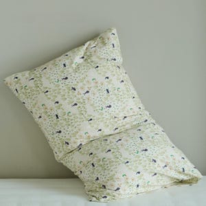 May include: A large, rectangular pillow with a cream-colored background and a repeating pattern of green leaves, small black birds, and tiny yellow flowers. The pillow is slightly crumpled, suggesting use and comfort.