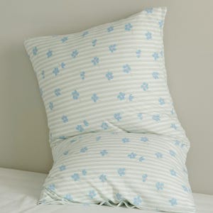 May include: A white pillowcase with a light blue floral pattern and thin, horizontal stripes. The pillowcase is filled and appears soft, with a slight curve. The floral pattern is scattered across the fabric.