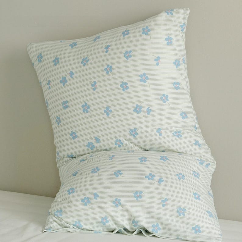 May include: A white pillowcase with a light blue floral pattern and thin, horizontal stripes. The pillowcase is filled and appears soft, with a slight curve. The floral pattern is scattered across the fabric.