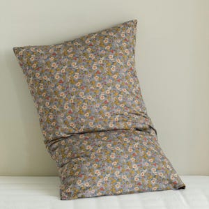 May include: A large, rectangular pillow with a floral pattern. The pillowcase is a muted gray color, covered in a repeating pattern of small yellow, orange, and white flowers. The pillow is resting on a white surface.