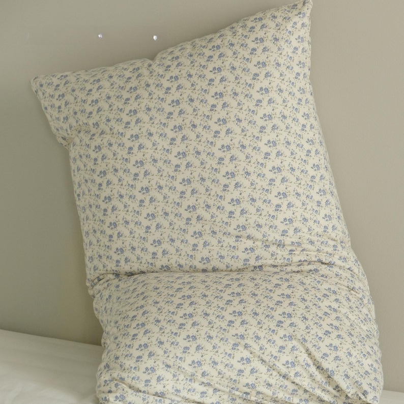 May include: A large, cream-colored pillow with a delicate floral pattern in light blue. The pillow is soft and appears to be made of a comfortable fabric, perfect for a bed or couch. The floral design adds a touch of elegance.