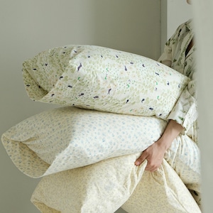 May include: Three decorative pillows with floral patterns. The top pillow has a green and white pattern with small black bird and plant illustrations. The middle pillow has a blue and white floral pattern. The bottom pillow is a light yellow with a small floral pattern.