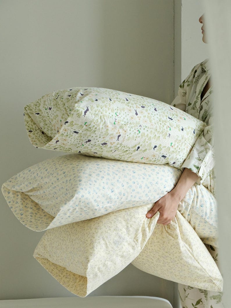 May include: Three decorative pillows with floral patterns. The top pillow has a green and white pattern with small black bird and plant illustrations. The middle pillow has a blue and white floral pattern. The bottom pillow is a light yellow with a small floral pattern.